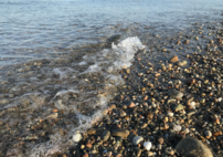 A close up image of small bubbles formed as a roughly 2 inch wave ripples from left to right over the gravel shoreline