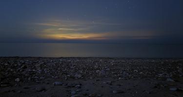 Rocky coastline at night, with the sun set just below the horizon