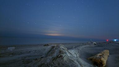 A picture of a shoreline at night, with the sun set just below the horizon, with the view running down the length of a piece of drift wood